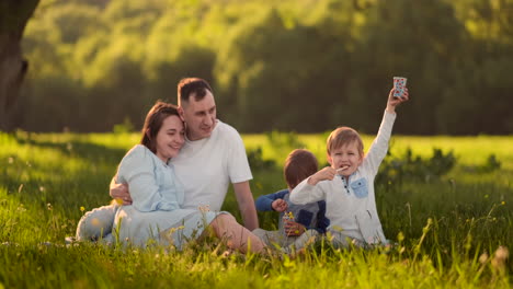 Loving-parents-hugging-sitting-in-the-field-at-sunset-and-looking-smiling-at-two-sons-eating-ice-cream-in-the-summer.